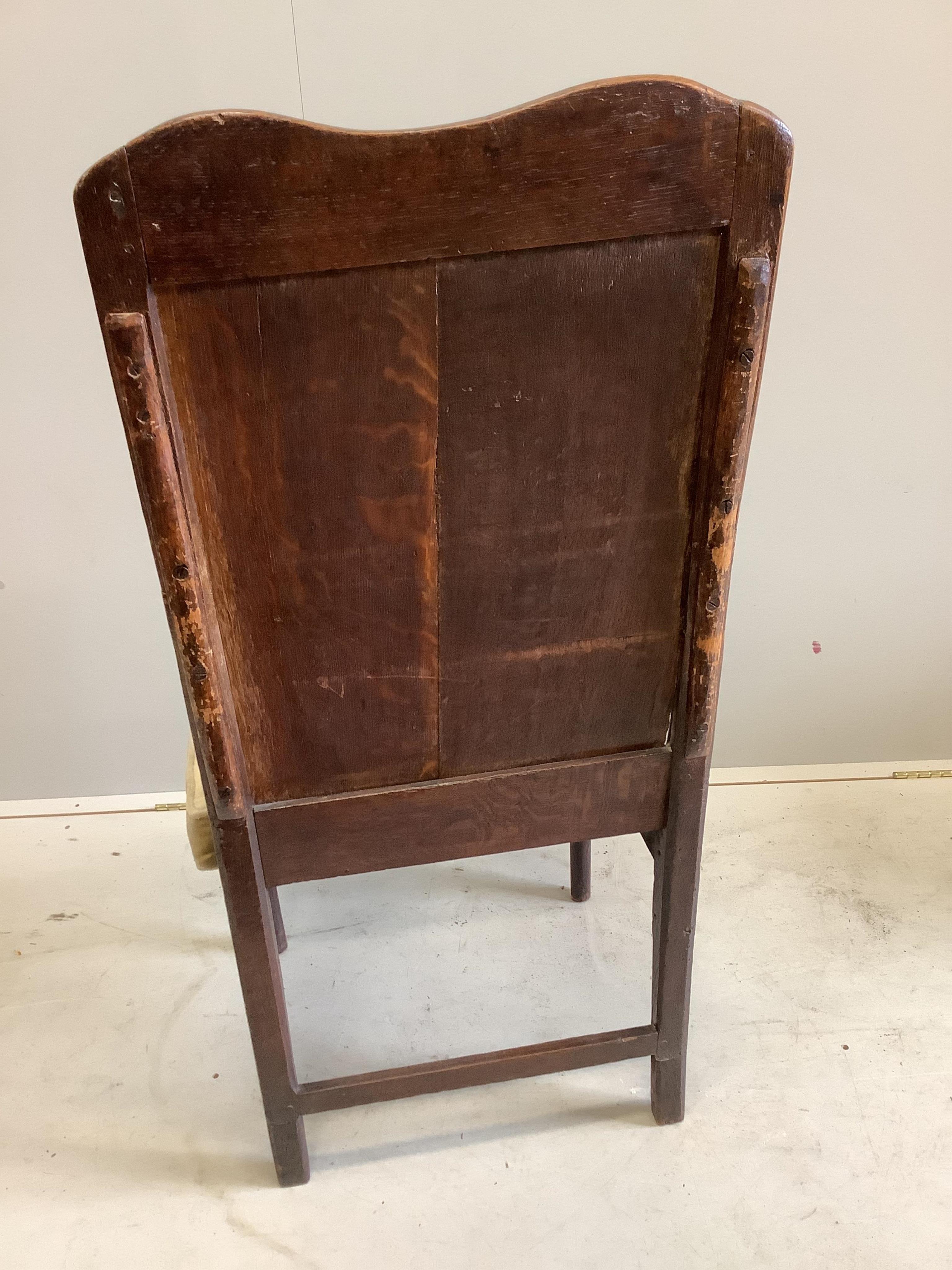 An early 18th century oak panel back open armchair, width 56cm, height 123cm. Condition - faded and worn with a missing drawer beneath the seat